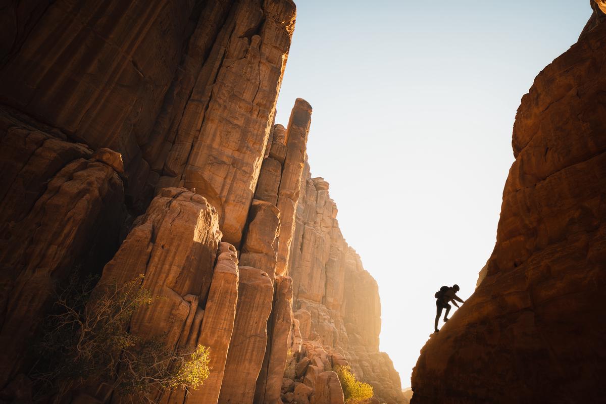 Illustration of a person climbing a mountain of debt with determination and a victory in sight.